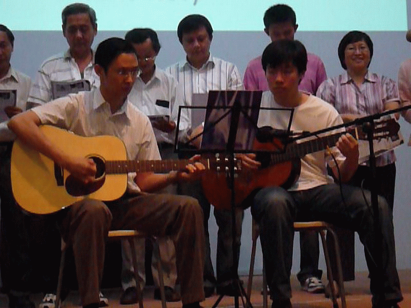 Winston Ho playing the guitar on stage during Thanksgiving celebration.